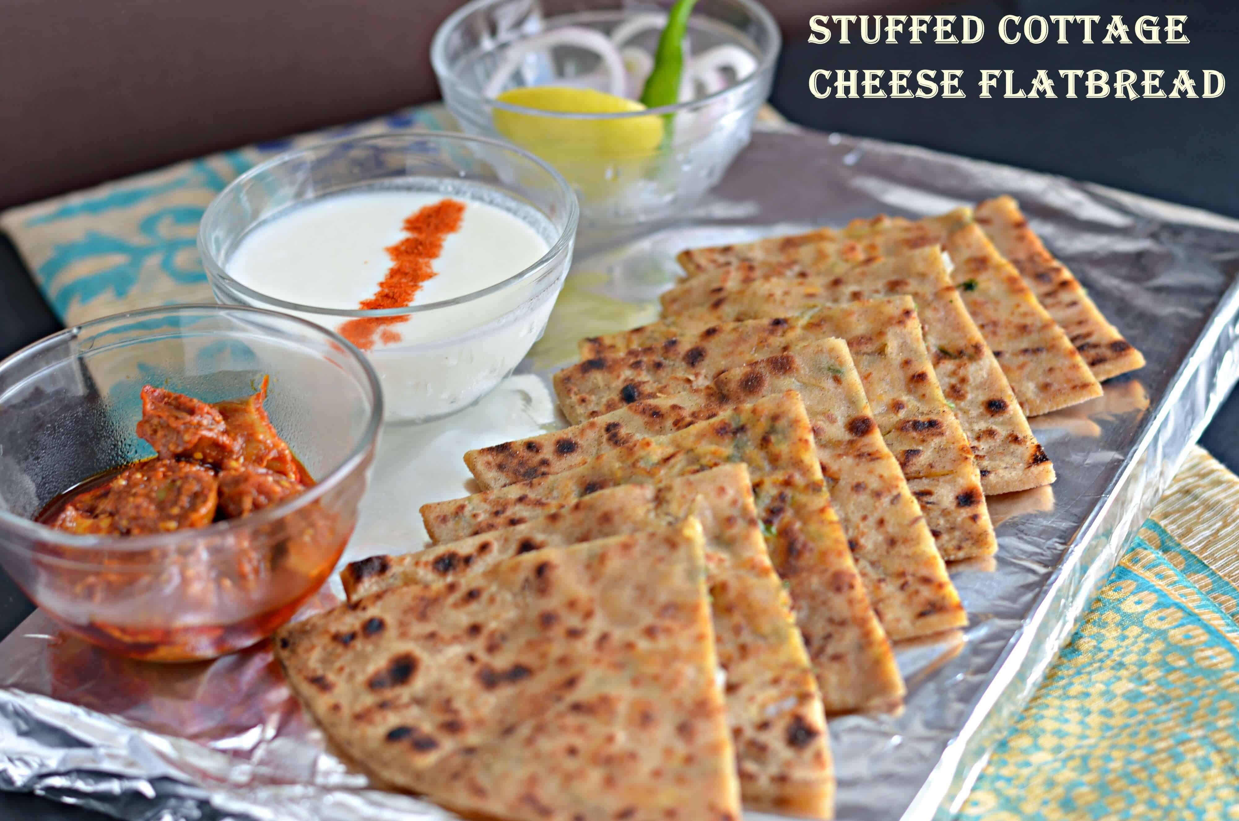 a side view of paneer paratha served with pickle, curd and onion slice.