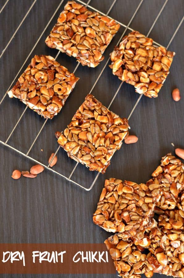 dry fruit chikki or mixed nut brittle bar is placed on rack, close up from above. Peanuts are scattered around.