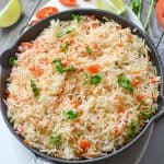spanish rice served in black pan with lemon wedges and chilies.