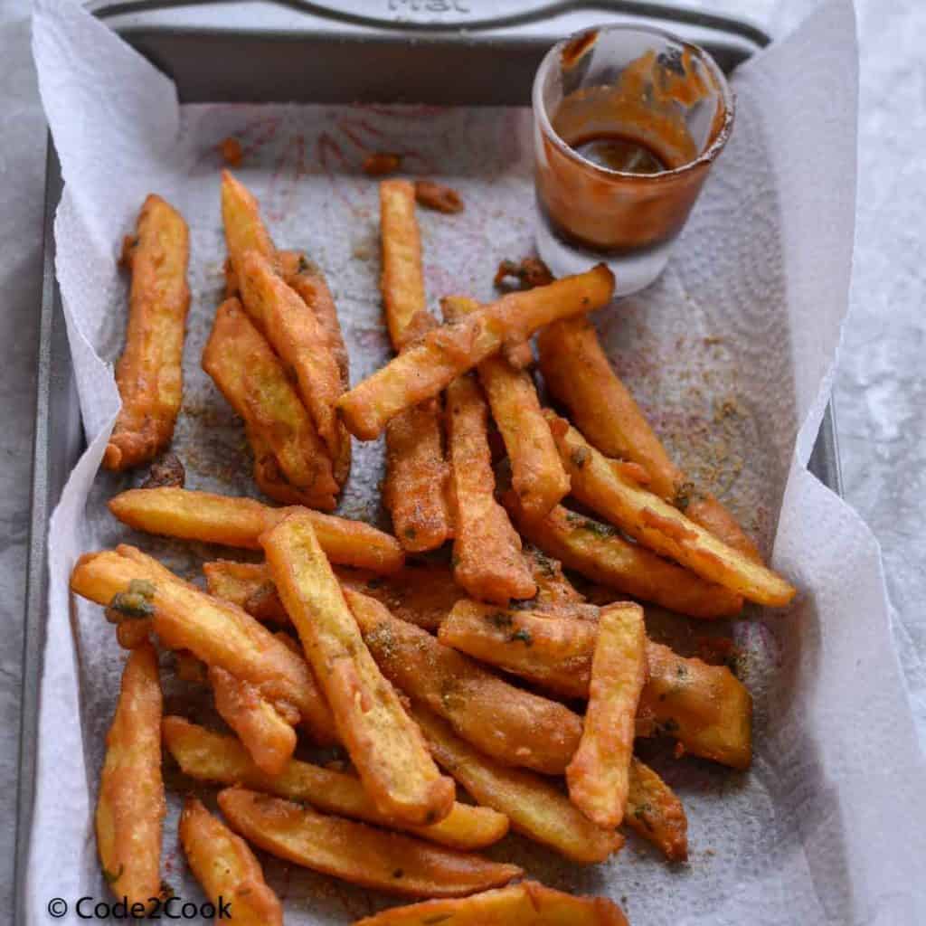 A close up click of farali french fries kept on baking pan. Tamarind chutney is also served along with fries.