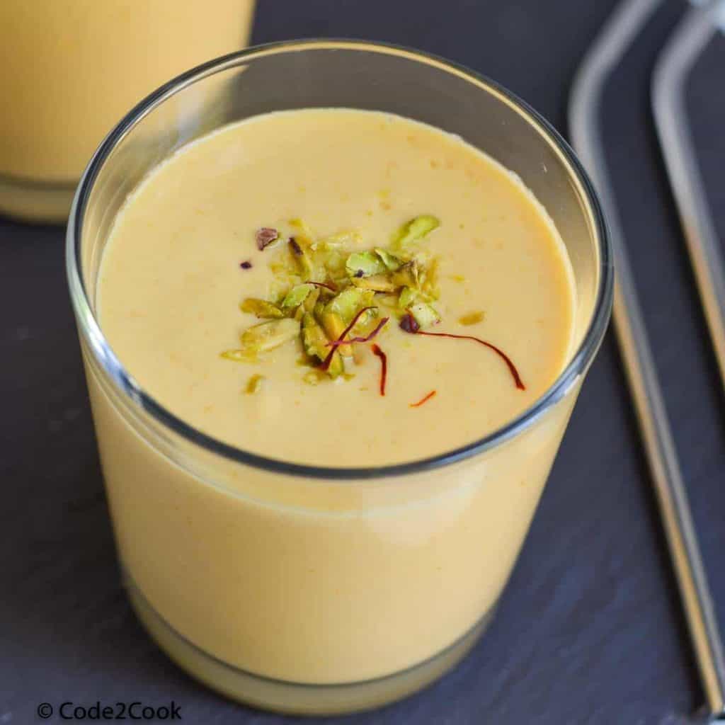 Mango lassi served in tall glass garnished with pistachio & saffron strands