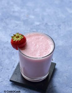 Rooh afza lassi served in a glass and garnished with strawberry