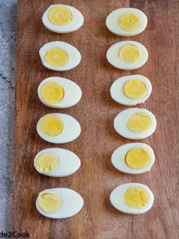 Boiled eggs cut in half and placed on wooden board. Table salt & pepper kept on left side.