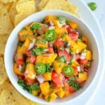 mango salsa served in white bowl with tortilla chips along side.