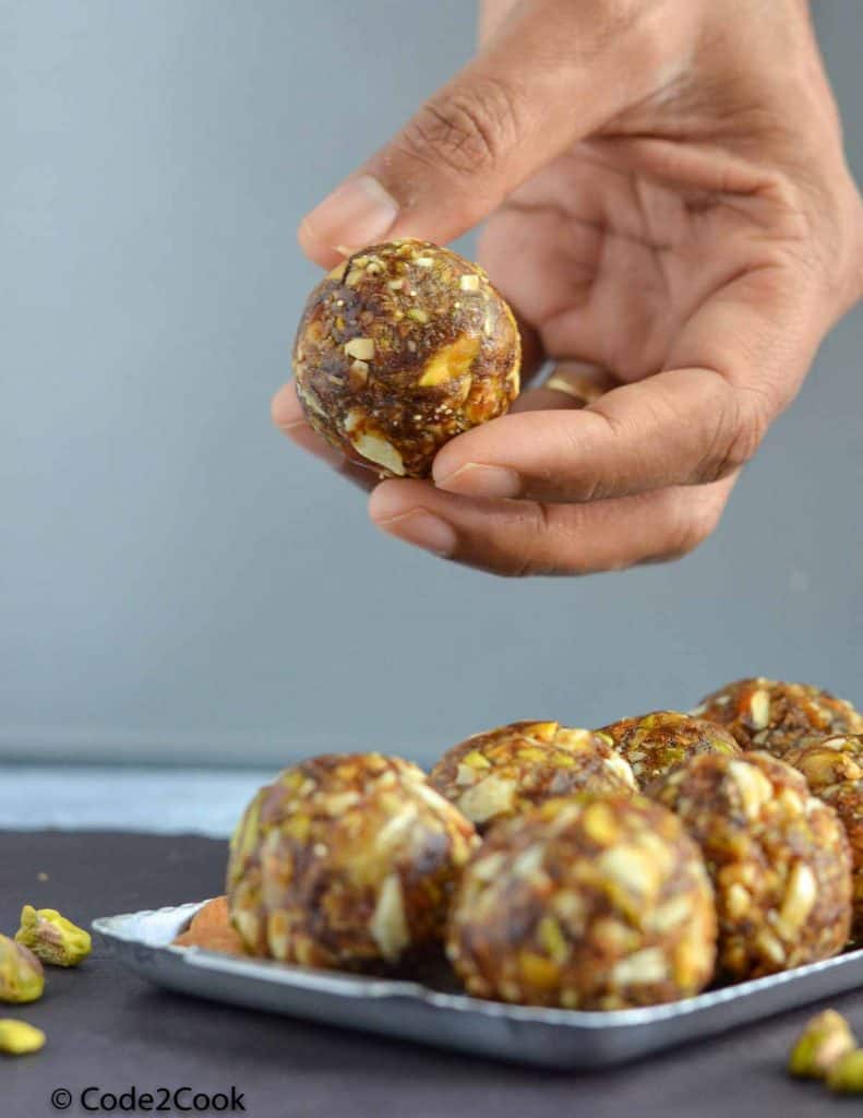 dry fruits laddu served in silver plate, and holding one