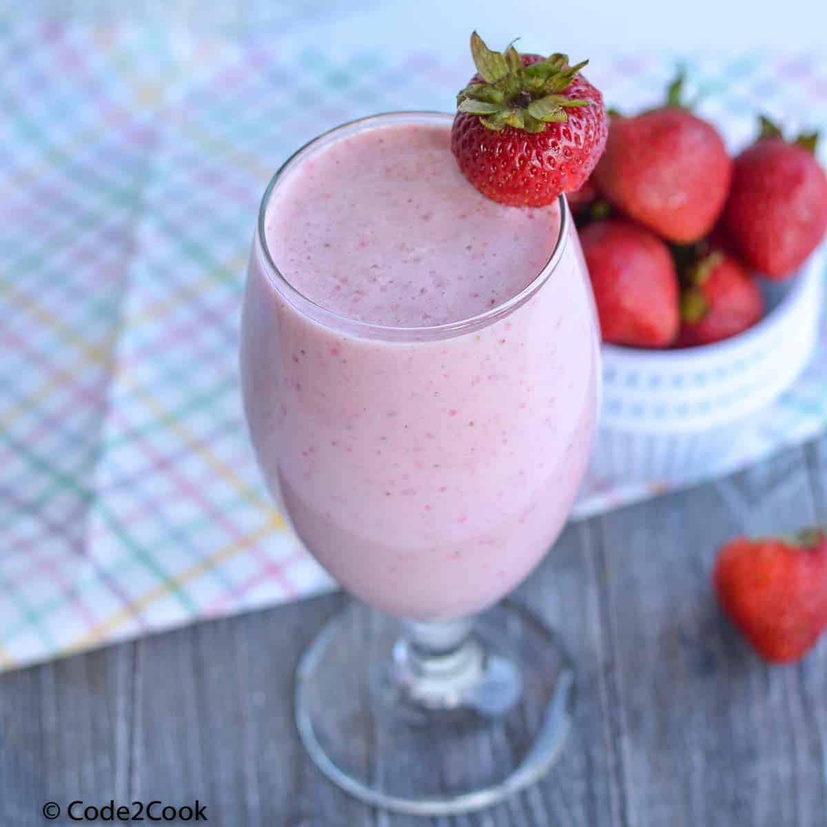 A close click of strawberry milkshake, strawberries lying behind the glass.