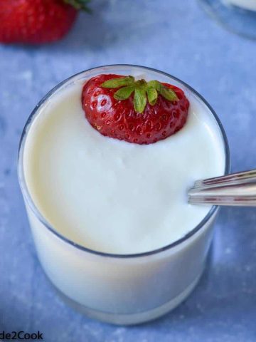 a close up shot of instant pot yogurt served in a glass with cut strawberries.