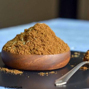 Ground cumin is kept in a wooden bowl with spoonful on right side.