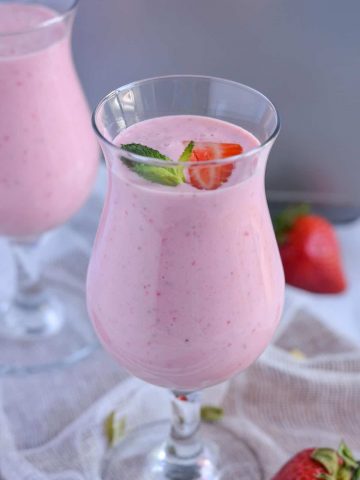 Close up click of strawberry lassi served in glasses and garnished with mint leaves